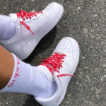White sneakers with bright red laces worn with white socks on a gravelly ground; casual footwear outdoors