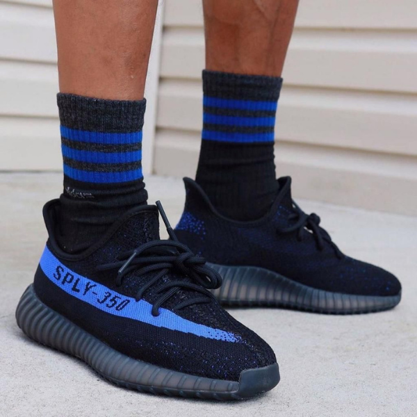 Close-up of black athletic sneakers with blue accents and 'SPLY-350' branding, worn with blue-striped socks on concrete ground.