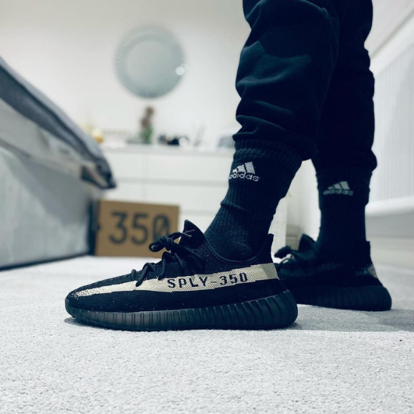 Close-up of black Adidas Yeezy Boost 350 sneakers with the SPLY-350 stripe on a carpet, box in the background