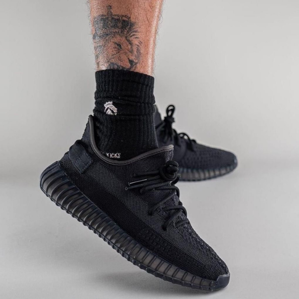 Close-up of a black knit sneaker on a foot, worn with a black sock, showcasing a ribbed, ridged outsole.