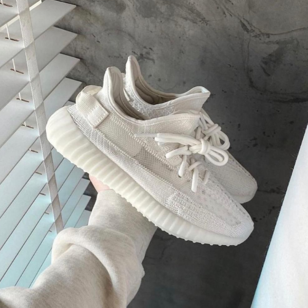 White knit sneakers with a chunky ridged sole held in a hand near window blinds