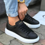 Untitleddesign-2022-06-02T083449.573_cf51bc4d-df90-40fe-b77d-226182cfb829 | UAE SPORT STORE Person tying black Alexander sneakers with a thick white sole, wearing rolled-up jeans and a gold watch on the wrist.
