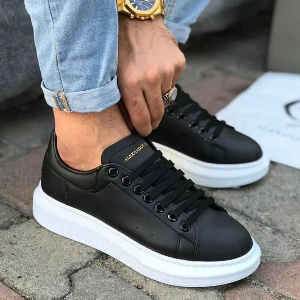 Untitleddesign-2022-06-02T083449.573_cf51bc4d-df90-40fe-b77d-226182cfb829 Person tying black Alexander sneakers with a thick white sole, wearing rolled-up jeans and a gold watch on the wrist.