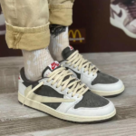 Pair of gray, white, and cream Nike sneakers with cream laces on a wooden floor; rolled khaki pants and white socks visible.
