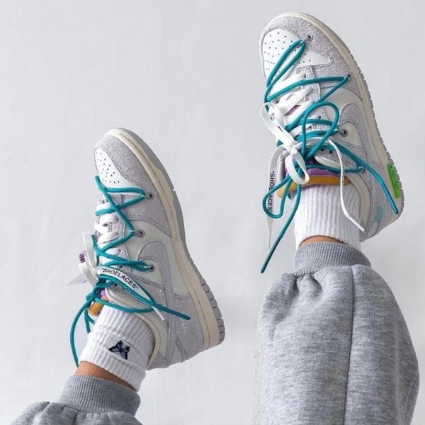 Two light gray sneakers with teal laces and white socks, shown raised against a light background (casual athletic look).