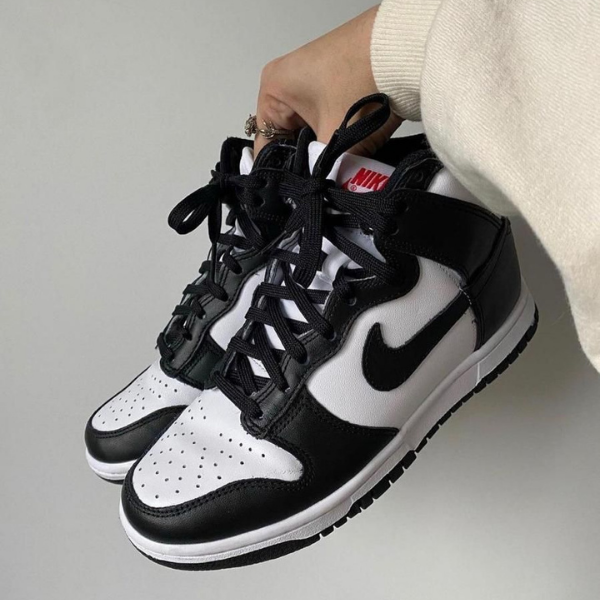 Pair of black and white Nike sneakers held by a hand, showing the swoosh and laces up close.