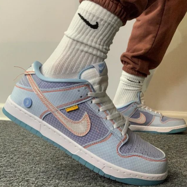 Person wearing light blue and pink Nike sneakers with white socks and a turquoise sole, standing on a carpeted floor