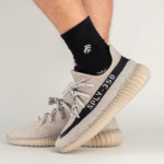 Beige knit sneakers with a thick beige sole and a black side stripe reading SPLY-350, worn with black socks nearby