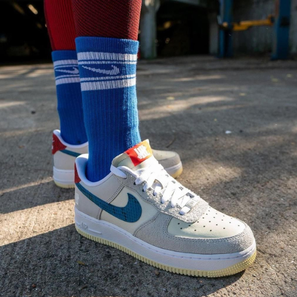 Child wearing white Nike Air sneakers with blue swoosh, blue socks, standing on pavement outdoors.