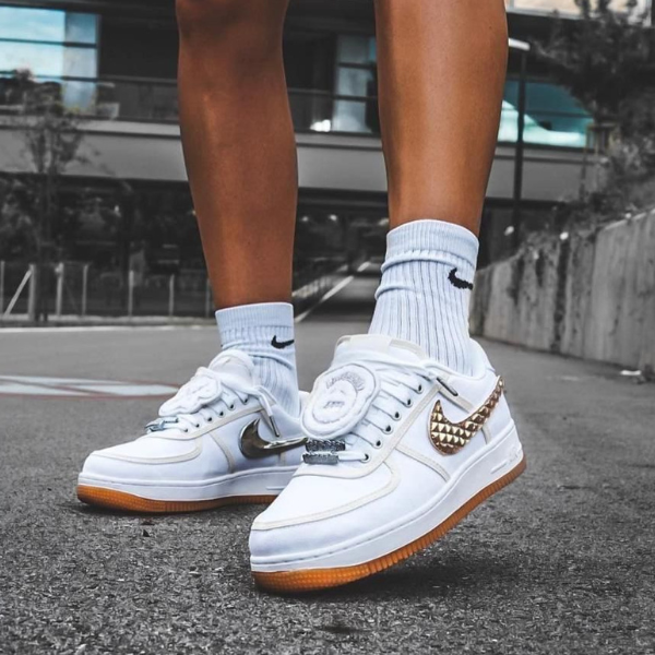 Close-up of white Nike sneakers with gum soles on gray pavement, worn with light-blue ribbed socks.