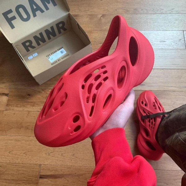 Red foam clog with numerous ventilation holes being held, with a matching red pair nearby and a Foam Runner box in the background