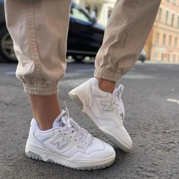 Person wearing white sneakers and beige jogger pants standing on a city street.