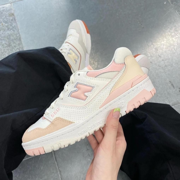 White and pastel pink New Balance sneaker held in hand, side view with N logo and perforated vamp image.
