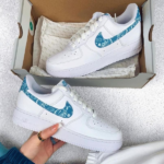 White Nike Air Force 1 sneakers with turquoise paisley swoosh, in a shoe box.