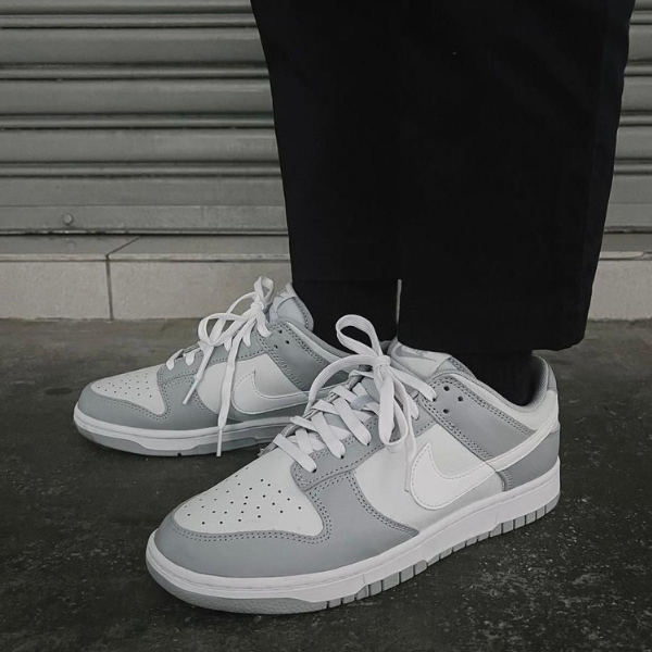 Close-up of gray and white Nike sneakers on a person standing on a dark pavement in front of a metal roll-up door.