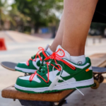 Green and white sneakers with bright orange laces resting on a skateboard at a skatepark edge.
