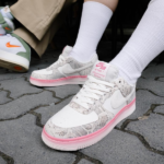 Close-up of white Nike Air sneakers with pink midsole worn with white socks, standing on a paved surface.