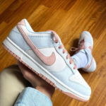 Pastel blue Nike sneaker with pink swoosh and pink laces held over a wooden floor.