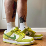 Person wearing lime-green Nike-style sneakers with white panels and lime laces, standing on a wooden floor with tattoos visible on the legs.