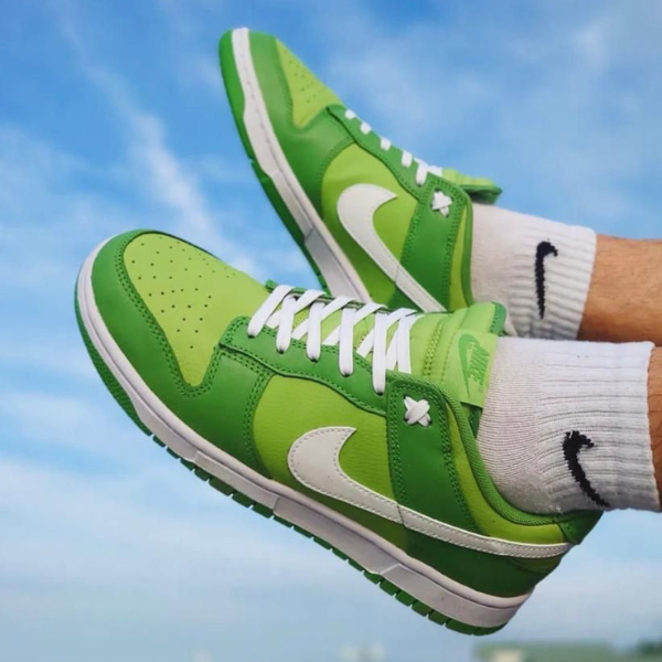 Pair of lime-green Nike sneakers with white swoosh and laces, worn with white socks against a blue sky.
