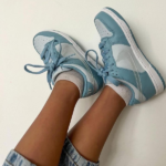 Feet in pastel blue and white sneakers with laces, resting against a light wall, wearing white socks and rolled-up jeans.