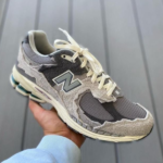 Gray New Balance running shoe with cream laces held in a hand, outer sole visible