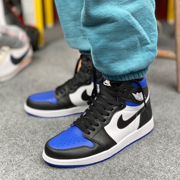Close-up of blue, black, and white high-top sneakers on a gray floor, with teal joggers visible at the ankles.