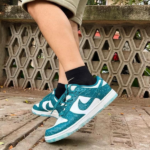 Feet in teal and white Nike sneakers on a concrete path, black socks, with a hexagonal lattice wall in the background.