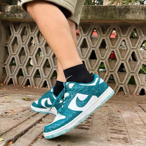 Feet in teal and white Nike sneakers on a concrete path, black socks, with a hexagonal lattice wall in the background.