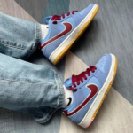 Blue sneakers with maroon Nike swooshes, white midsole and gum outsole, worn with jeans.