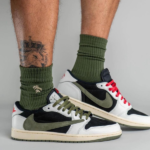Pair of white, black, and olive sneakers with green laces and red accents, worn with olive socks, shown from the ankles down.
