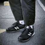 Untitleddesign-2023-01-05T122658.777_7923b299-25ea-40cc-b2ed-c2215a2d69c3 | UAE SPORT STORE Pair of black New Balance sneakers with white socks standing on a street or parking lot surface.