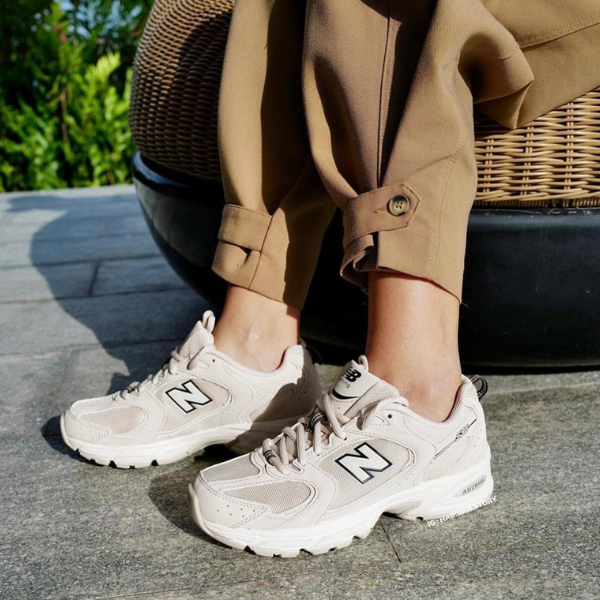 Untitleddesign-2023-01-05T123700.645_3a44b788-3f4c-4268-a8c6-d1447da304ee Person wearing beige pants and cream New Balance sneakers standing on a stone patio with a wicker chair nearby