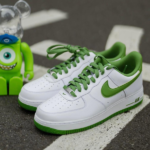 White Nike Air sneakers with green laces and green swoosh on a road, next to a green toy figure.