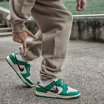 Close-up of a person in beige joggers tying turquoise and white Nike sneakers on a paved surface.