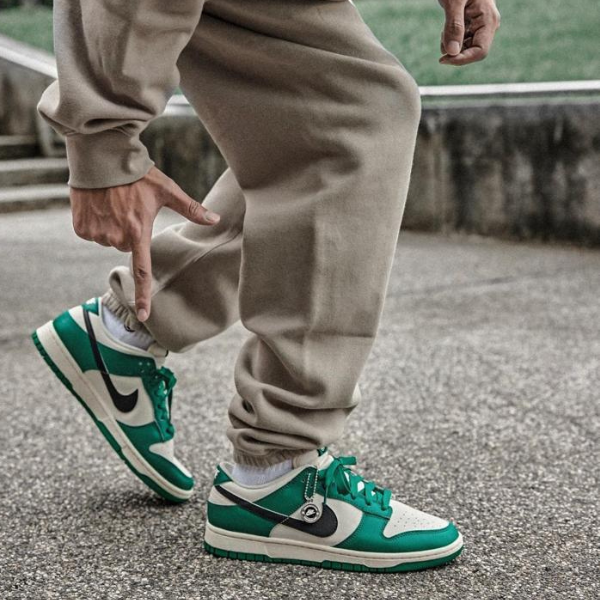 Close-up of a person in beige joggers tying turquoise and white Nike sneakers on a paved surface.