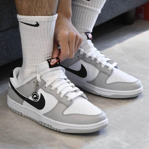 Person tying white and gray Nike sneakers with black swoosh, wearing white socks nearby on a concrete floor.