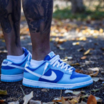Pair of blue Nike sneakers on a person standing outdoors among fallen autumn leaves. (Note: concise, informative alt text for an informative image.)