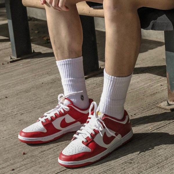 Red and white Nike sneakers worn with white crew socks, shoes resting on a concrete outdoor surface beside a bench.