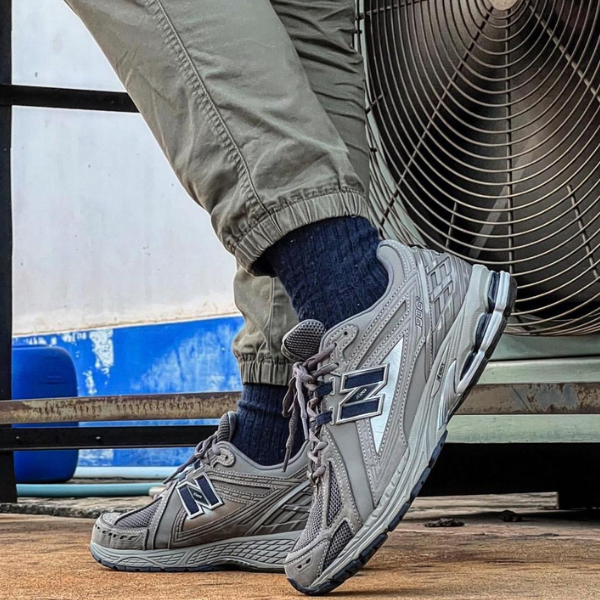 Close-up of gray New Balance running shoes on a person standing on a wooden surface beside a large outdoor fan.