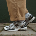 Close-up of someone wearing gray and black New Balance running shoes with tan cuffed pants standing on a concrete sidewalk.