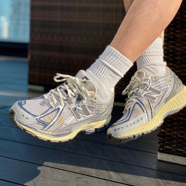 Gray and beige athletic sneakers on a person’s feet with white socks, resting on a wooden deck.