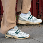 Untitleddesign-2023-02-09T122815.559_85deb89d-0494-4256-831e-82da96f83d1c | UAE SPORT STORE Pair of white and gray New Balance running shoes with green NB logo, worn with tan pants on a sidewalk.