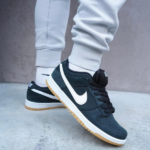 Close-up of navy Nike sneakers with white swoosh and gum-colored outsole, paired with gray joggers and white socks.