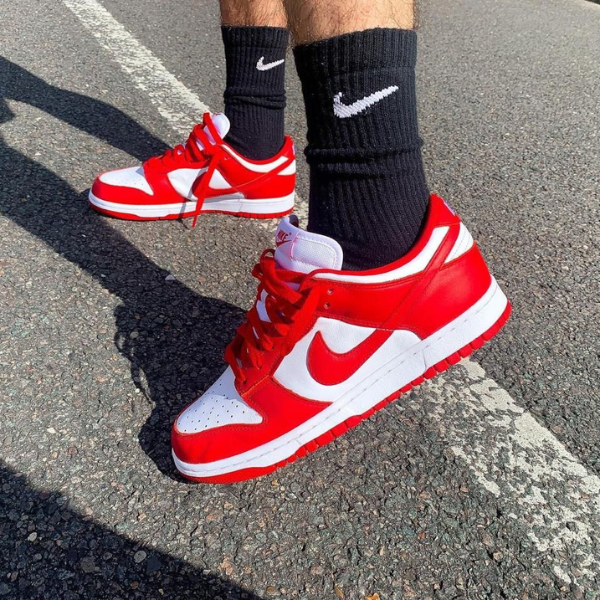 Red and white Nike sneakers on a person wearing black crew socks, standing on asphalt.