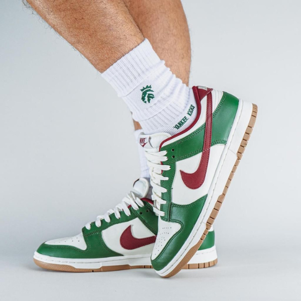 Untitleddesign-2023-11-08T055524.524_b16f2c1e-3ee3-453c-ab6d-442a0f66e91d White and green high-top sneakers with a red swoosh, laces tied, and a gum sole on white socks.