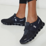 Person wearing black On running sneakers with a distinctive segmented hollow sole on a light floor surface