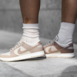 Person wearing beige Nike sneakers with white socks standing on a concrete surface.