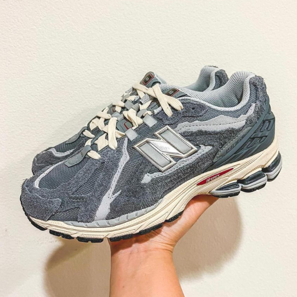 Gray New Balance running shoe held in a hand, showing a mesh and suede upper with white laces and a chunky cushioned midsole.