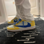 Child wearing yellow, white, and blue Nike sneakers standing on a dark rug indoors.